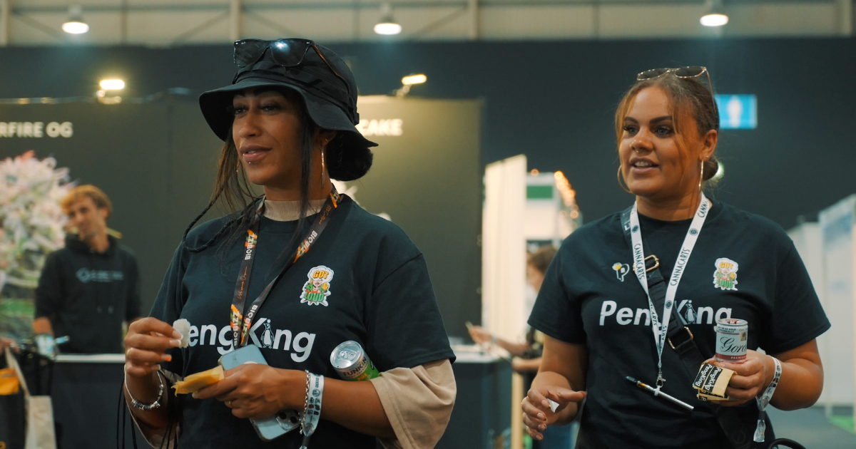 Two women at an expo, one wearing a black hat