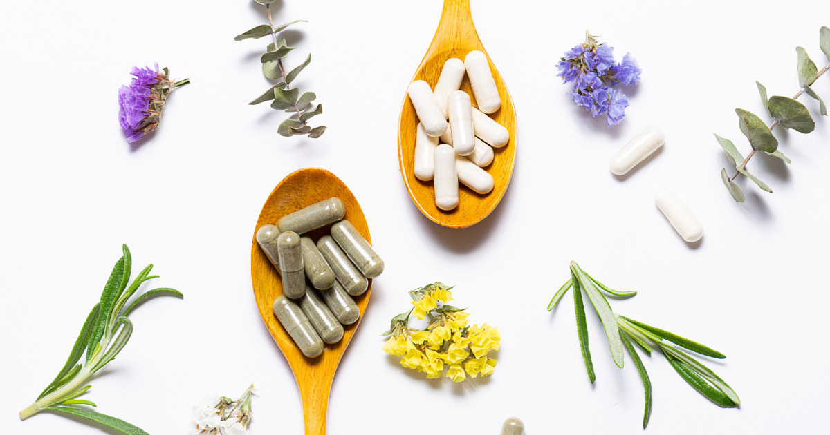Two wooden spoons with capsule tablet mushroom supplements, on a white background surrounded by flowers and greenery