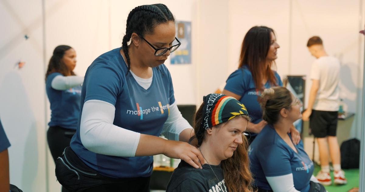 A woman with a headband sat down, being given a massage by another woman wearing glasses